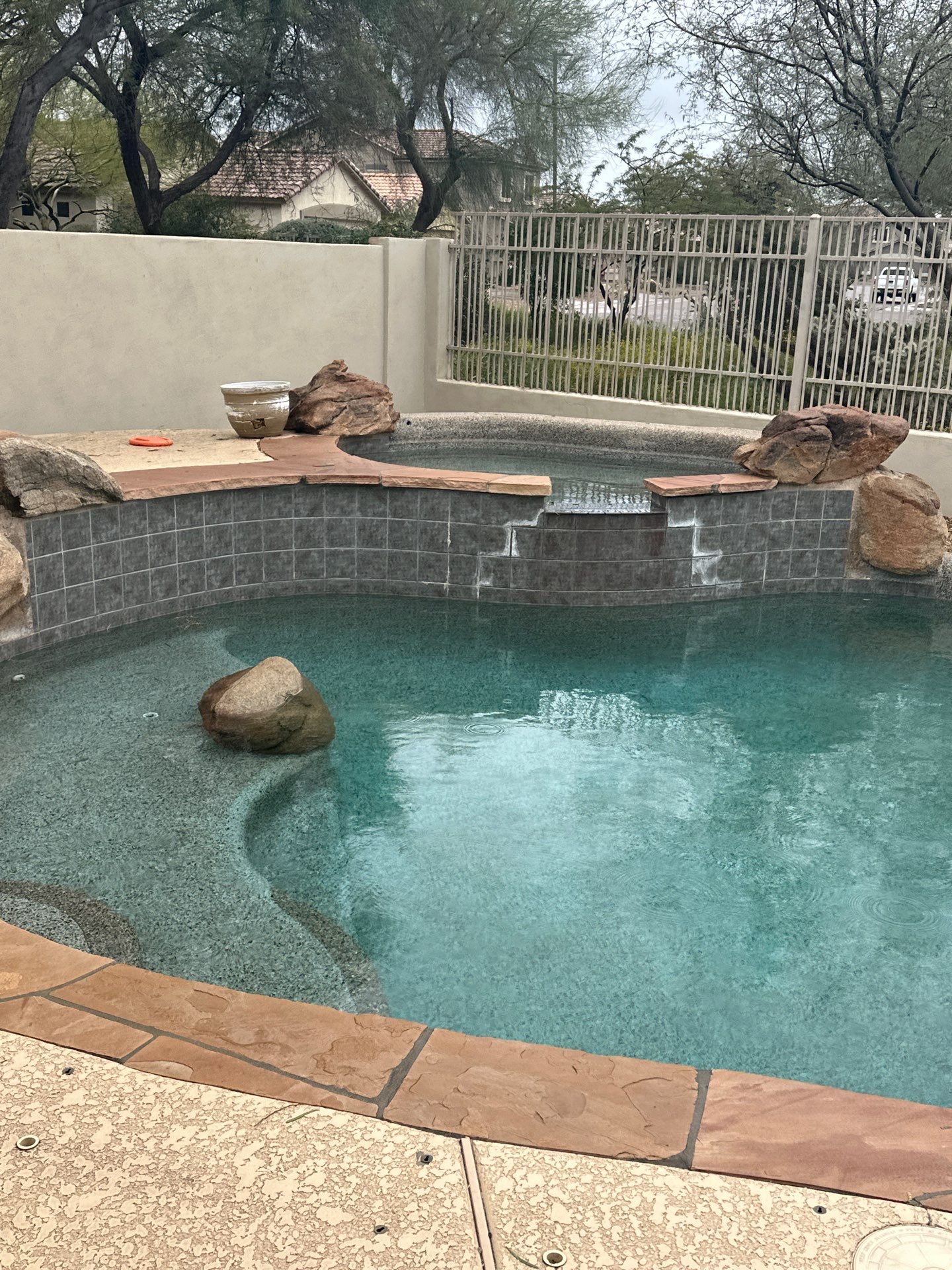 A turquoise swimming pool with an integrated raised spa, stone coping, and natural rock accents.