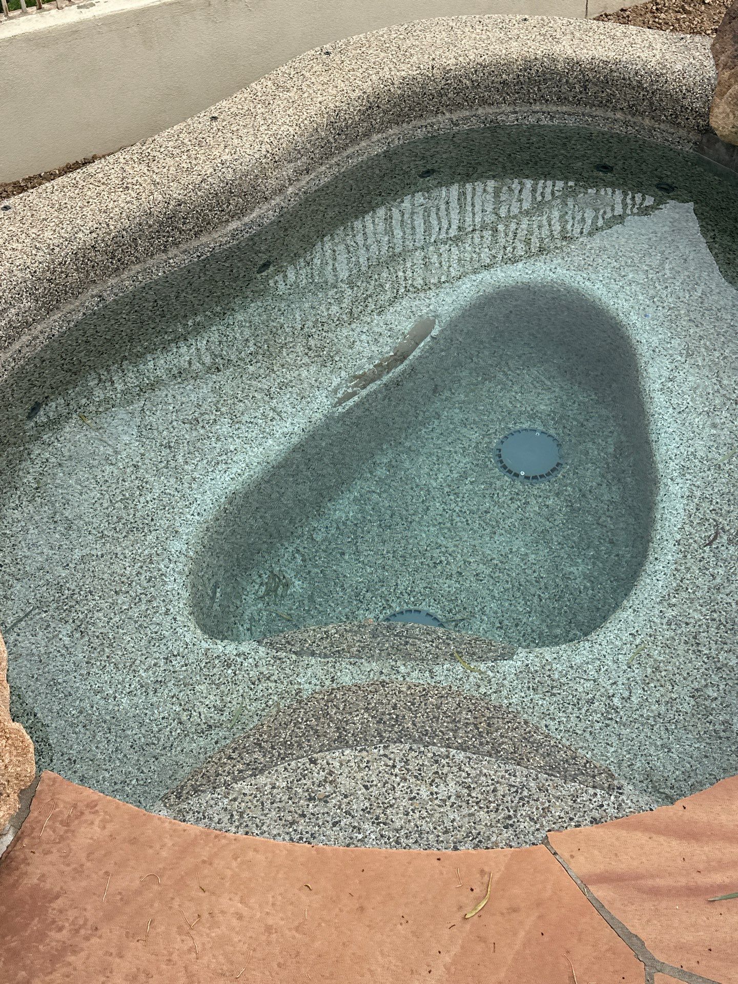 High-angle view of a pebble-finish concrete hot tub with built-in steps and clear water.