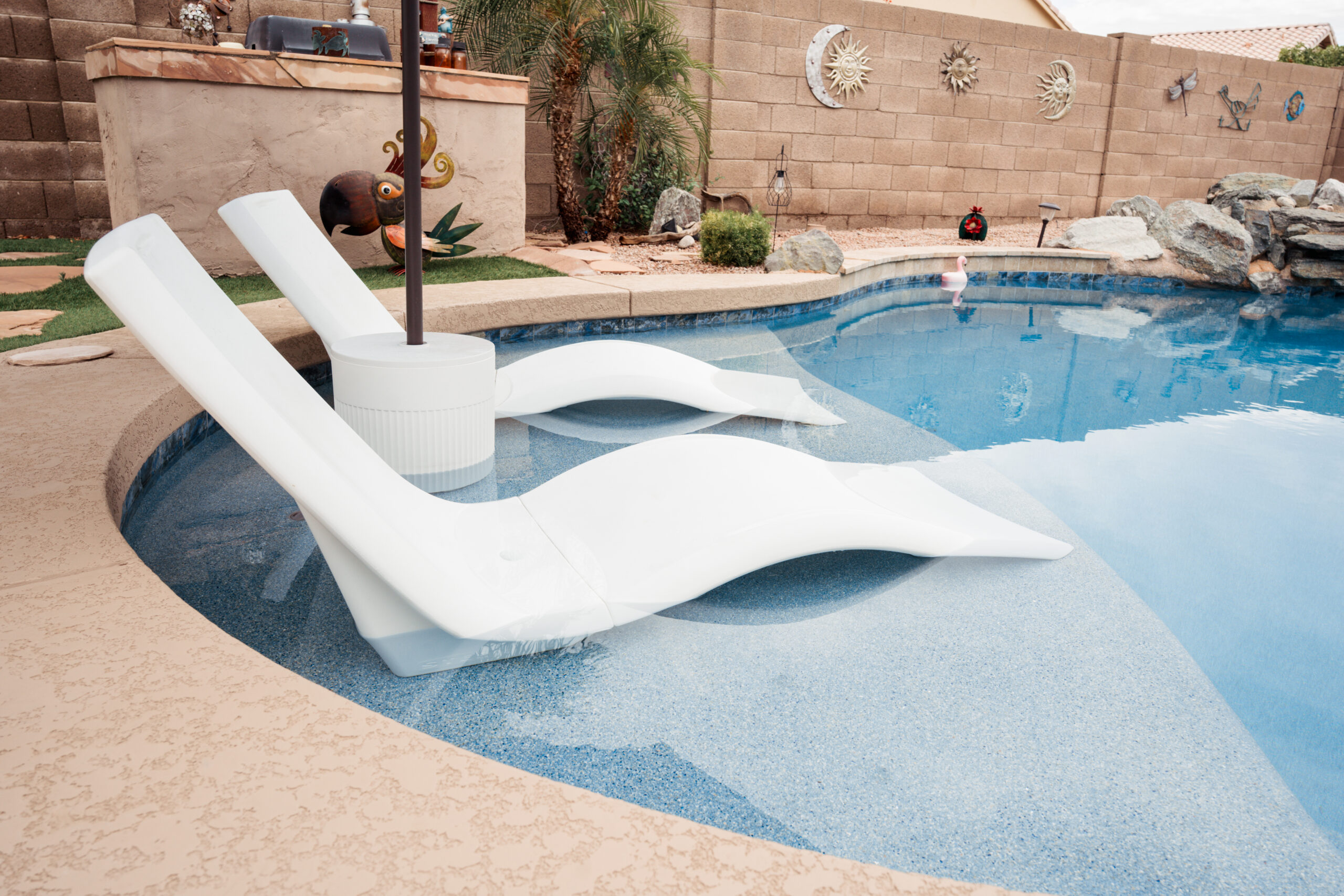 Two white modern lounge chairs partially submerged in a swimming pool's tanning ledge.